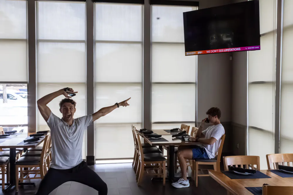 Maverick Digital team member at a partner café with an indoor advertising screen on the wall