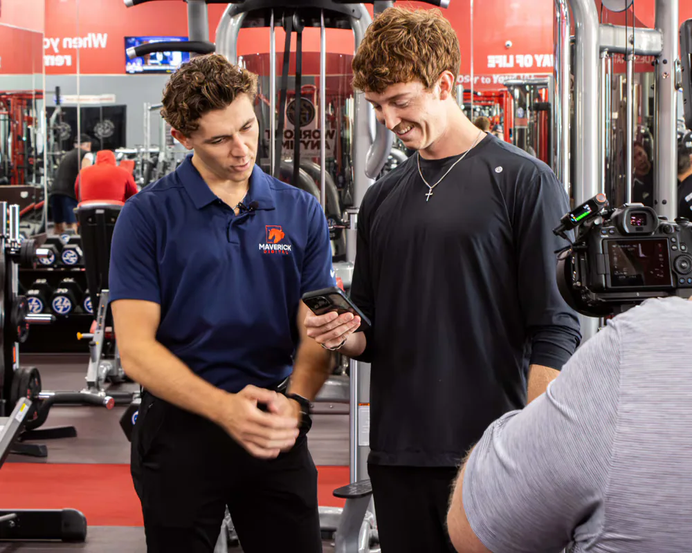 Maverick Digital team member reviewing ad content on a phone with a client during a gym video shoot