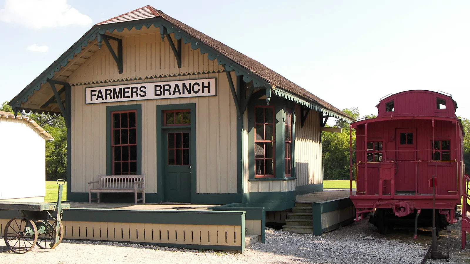 The original Farmers Branch railroad depot, a cream and green wooden station with its name sign, beside a red caboose and an old baggage cart