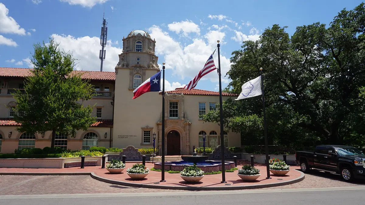 Highland Park Town Hall, a Spanish-style building with a domed tower, with the Texas, US and town flags flying over the fountain out front