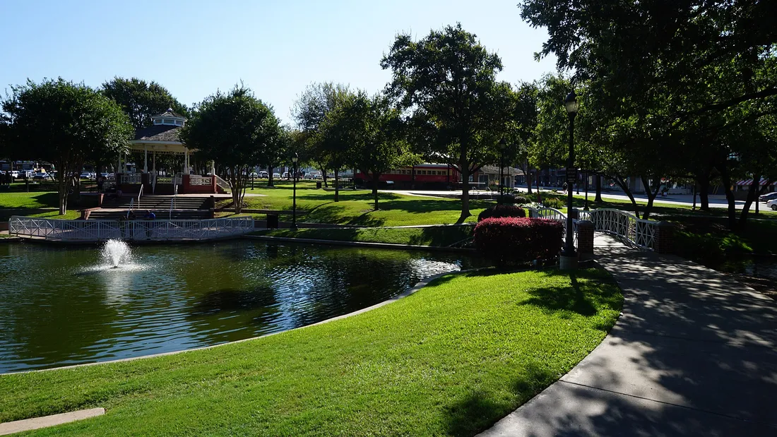 Haggard Park in downtown Plano: a pond with a fountain, a white gazebo, and a red vintage interurban railcar beyond the trees