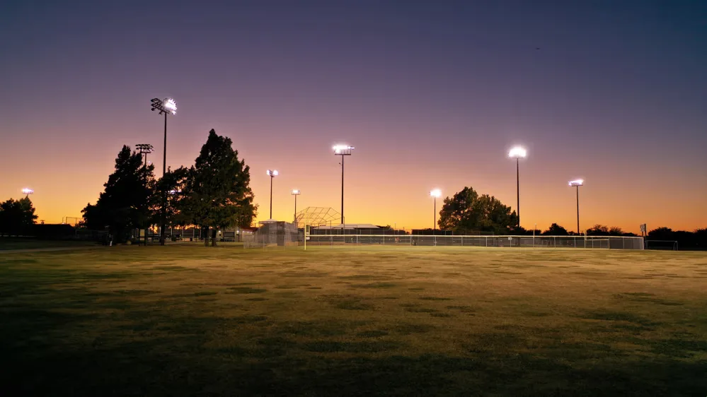 Floodlit sports fields at dusk under an orange and purple sky