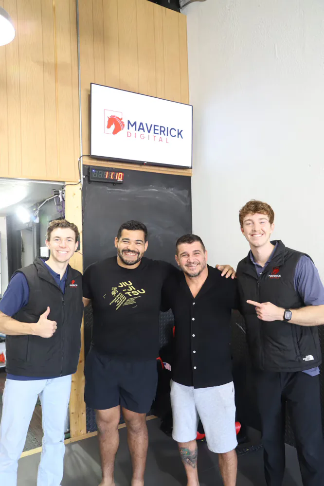 Maverick Digital team with a venue partner beneath an indoor billboard advertising screen