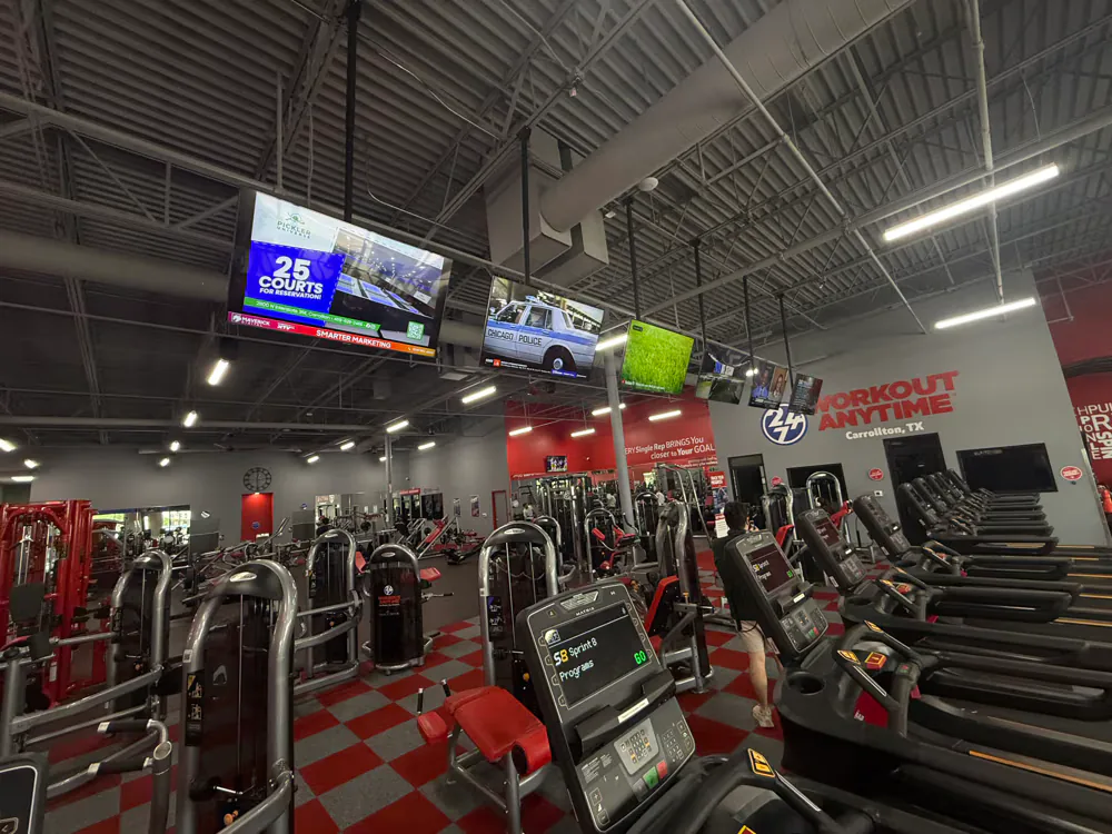 Indoor digital billboard screens above the cardio floor of a Carrollton gym